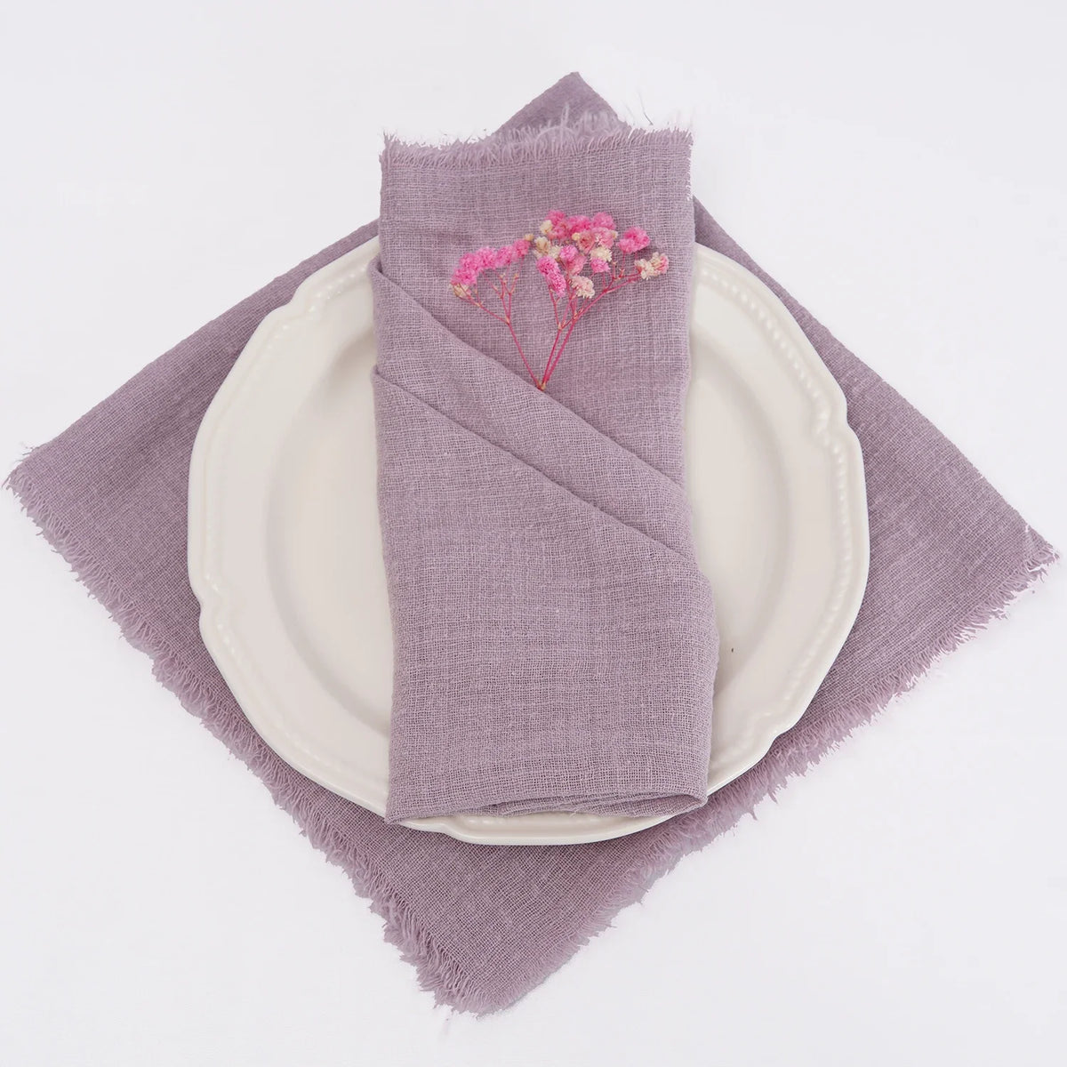 A stack of purple linen napkins with pink floral accents resting on a lavender cloth and a white plate.