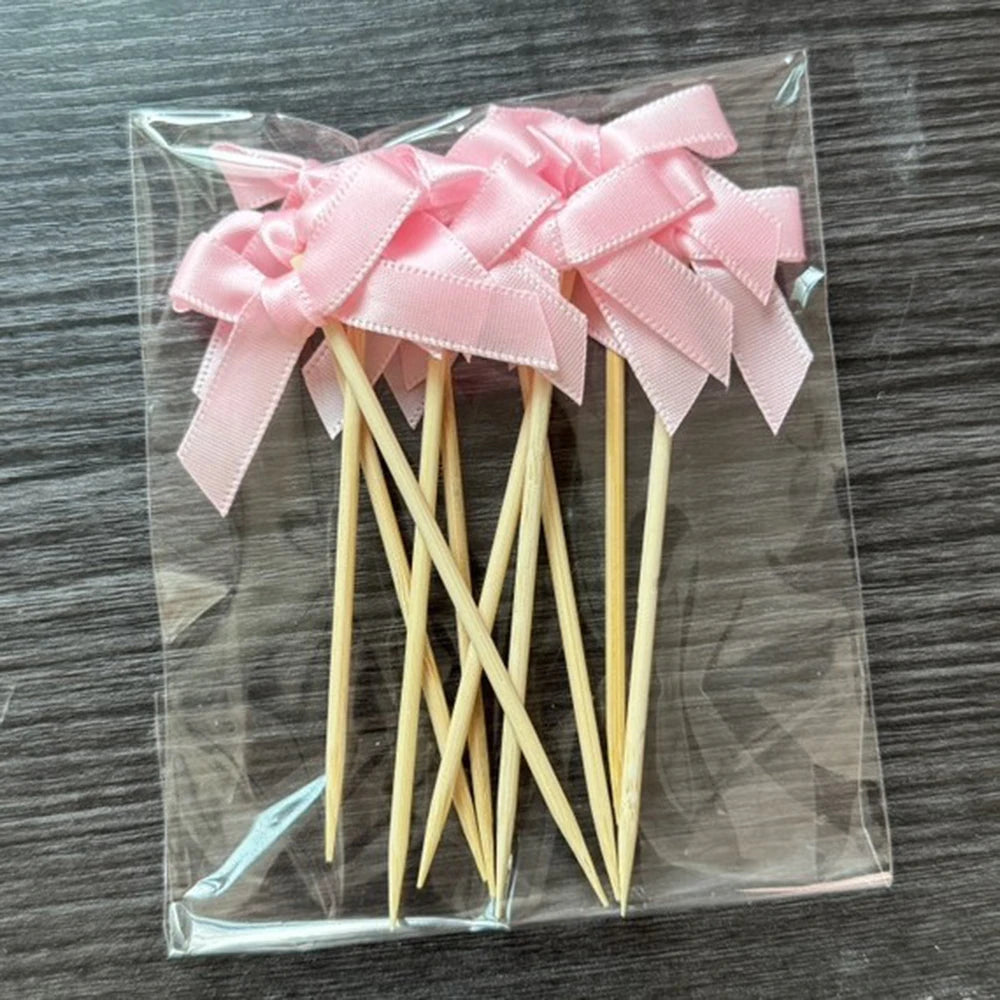 A set of pink bow cupcake toppers on wooden sticks packaged in a clear plastic bag.