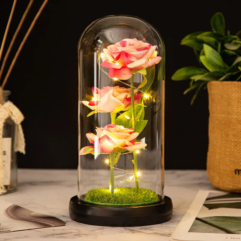 An LED galaxy rose artificial flower displayed inside a glass dome on a black base.