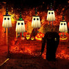 Halloween hanging ghost lights with witch hats illuminating a brick wall and orange pumpkins in a dark garden setting