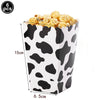 A black and white cow print paper cup filled with popcorn, used for a farm-themed party display.