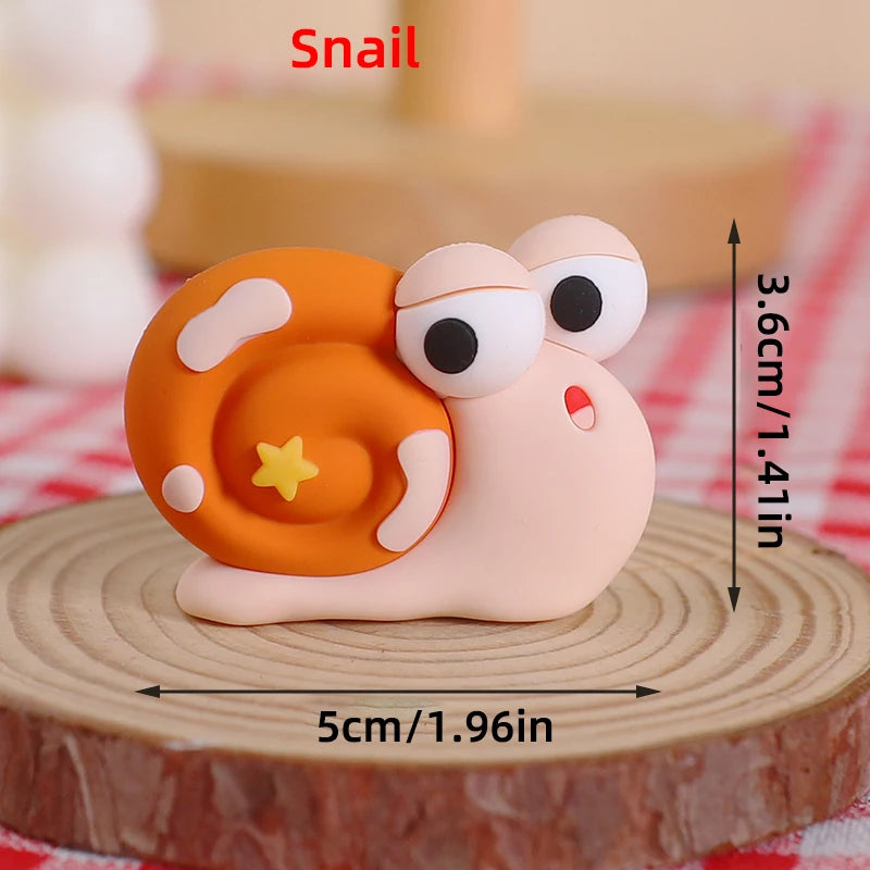 A small, round snail-shaped cake topper in orange and pink clay is displayed on a wooden surface.