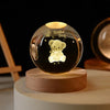 A glass crystal ball decoration with a glowing light inside, featuring a small teddy bear engraved on the surface.
