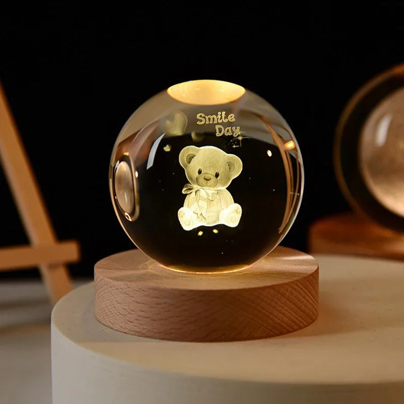 A glass crystal ball decoration with a glowing light inside, featuring a small teddy bear engraved on the surface.