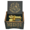A dark wooden box containing a brass music box with an engraved design of a leaping animal and celestial elements.