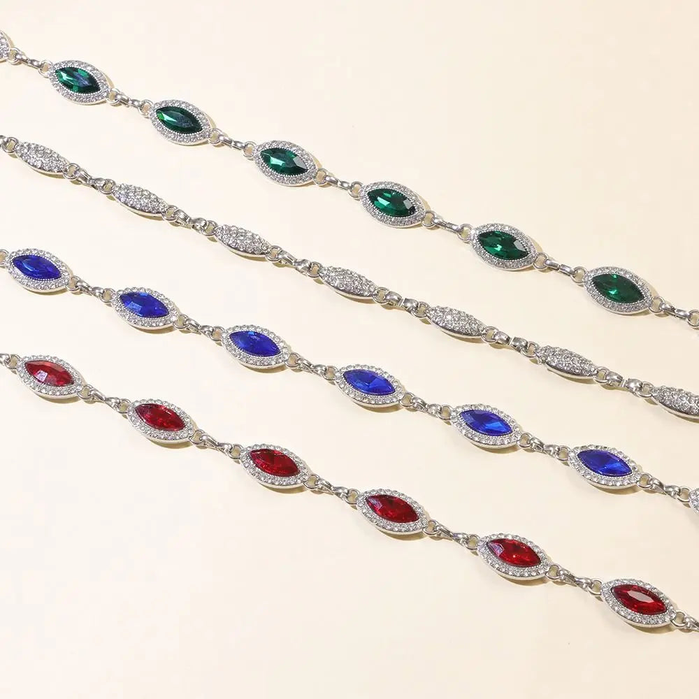 A display of colorful crystal waist chains featuring emerald green, sapphire blue, and ruby red gemstones.
