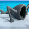 A gray 3D printed articulated sea monster fidget toy resting on a white surface with a bright blue ocean background.