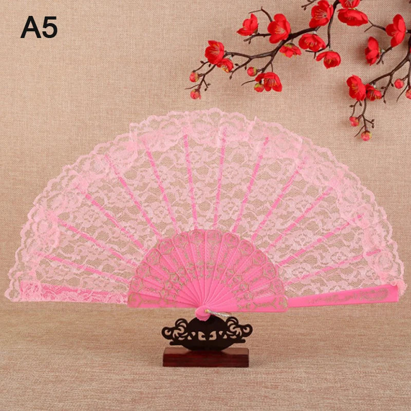 Pink lace folding hand fan with a fan shape and decorative base against a beige background.