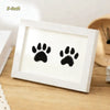 A white wooden photo frame displaying two black paw prints on a light brown wooden surface.