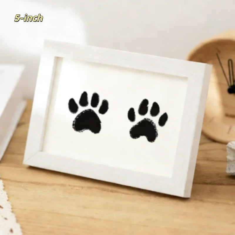 A white wooden photo frame displaying two black paw prints on a light brown wooden surface.