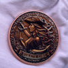 A copper challenge coin featuring a pirate girl design with flowing hair and an eyepatch.