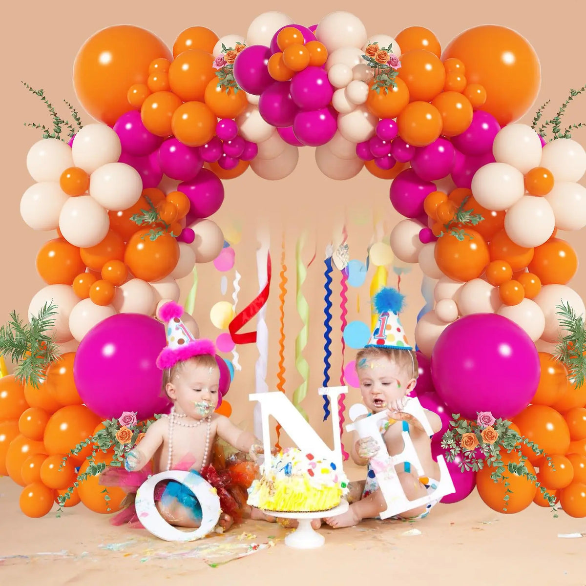 A balloon garland arch featuring pink and orange balloons decorated with flowers and a cake, surrounded by two babies.