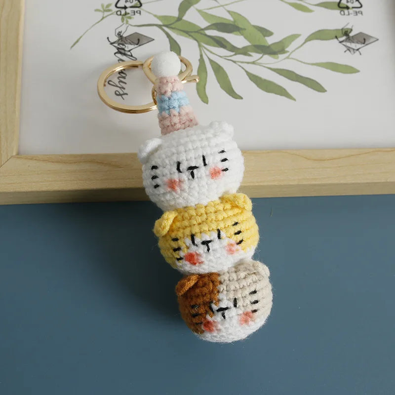 Handcrafted crochet cat keychain pendant featuring three small cats in white, yellow, and brown yarn.