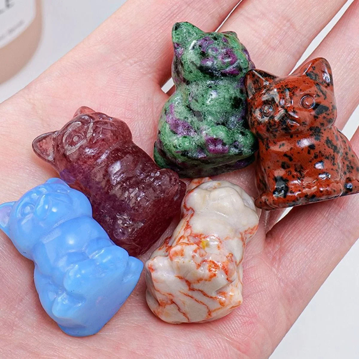 Collection d'ornements de chats en cristal sculptés à la main, dans diverses couleurs (vert, brun-rouge et bleu), posés sur u