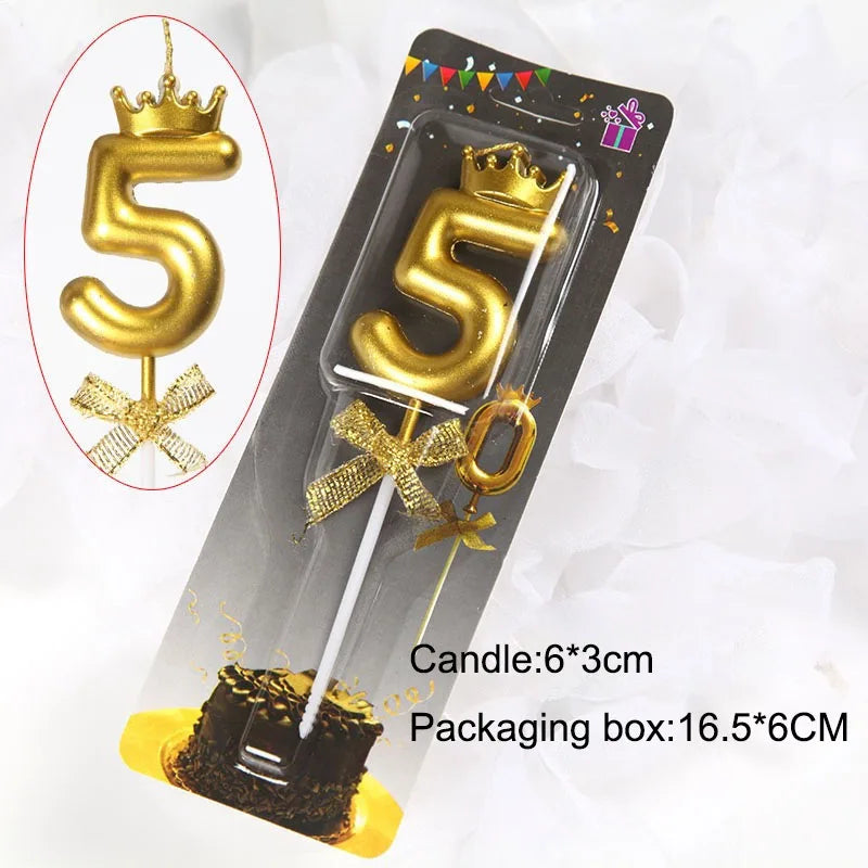 A gold number 5 candle in a packaging box with a crown topper and ribbon, displayed against white fluff.