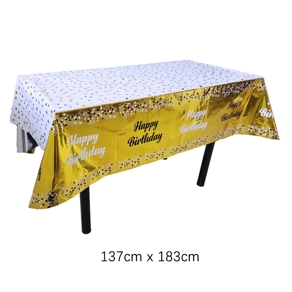 Una mesa de fiesta desechable rectangular dorada cubierta con tela de lunares blancos y decoraciones de cumpleaños.