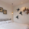 A white bedroom wall features a set of black metal hummingbird wall decor mounted on the wall.