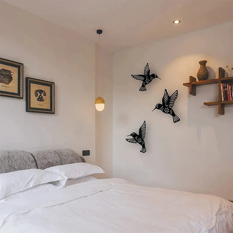 A white bedroom wall features a set of black metal hummingbird wall decor mounted on the wall.