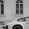 Une voiture moderne blanche est garée devant un bâtiment aux grandes fenêtres cintrées.