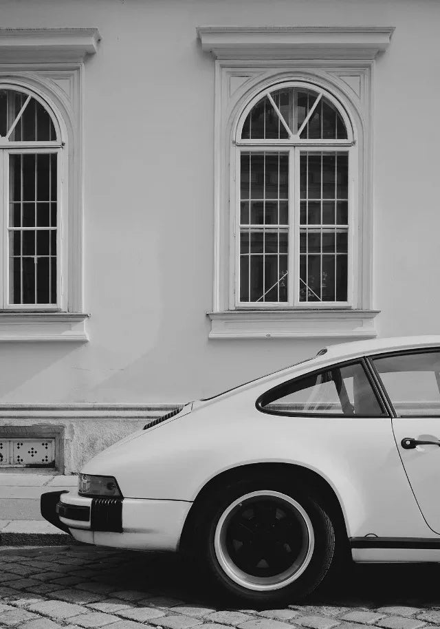 Une voiture moderne blanche est garée devant un bâtiment aux grandes fenêtres cintrées.