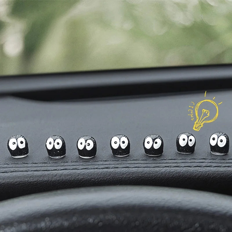 Une rangée de décorations pour voiture elfiques noires avec des visages surpris sur une surface sombre.