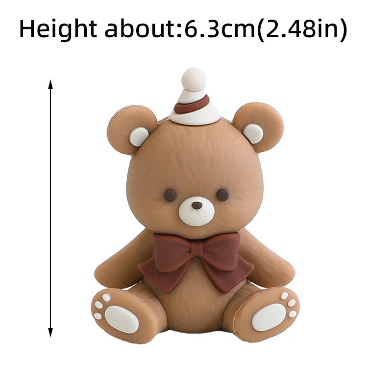 A cute brown teddy bear cake topper with a white conical hat and a brown bow.