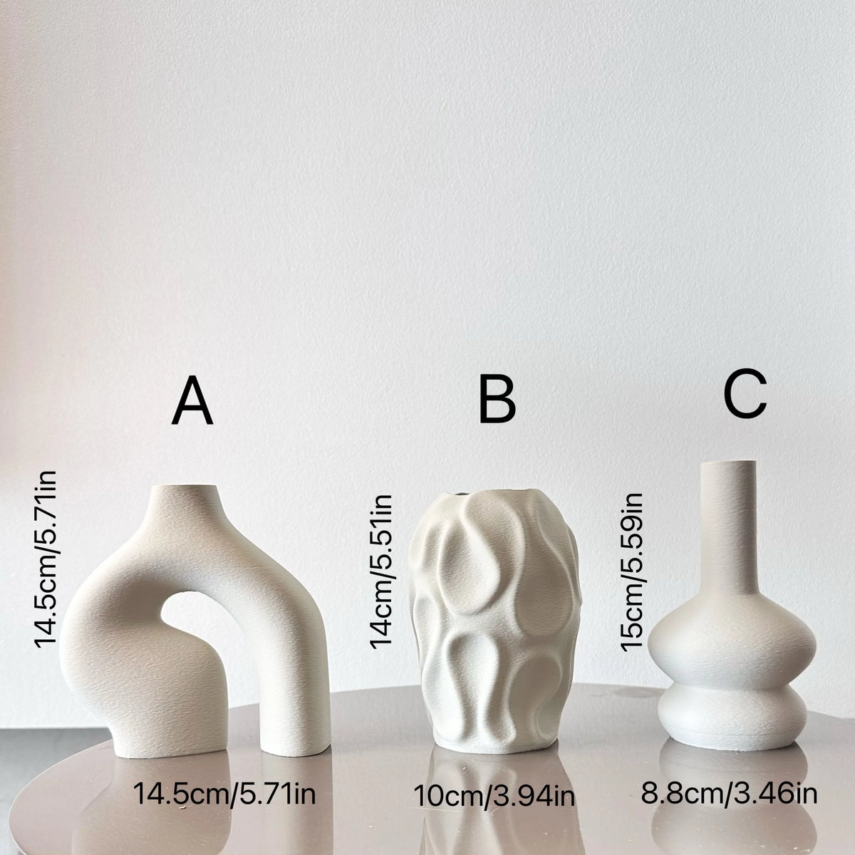 Three white ceramic geometric vases of varying heights displayed on a white surface.