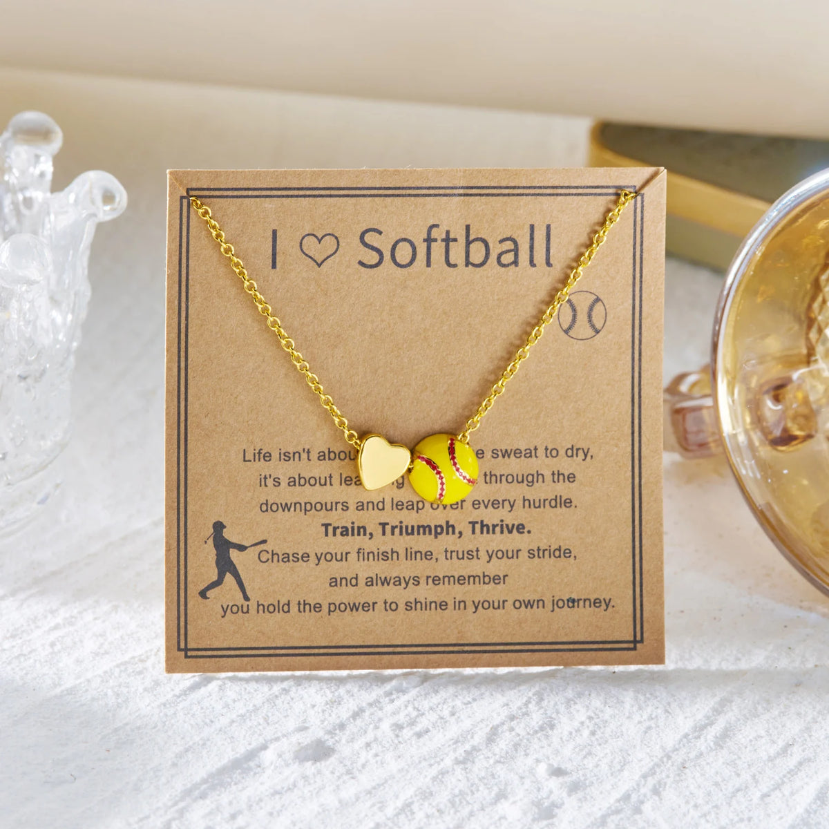 Gold heart pendant necklace with a softball charm on a brown card.