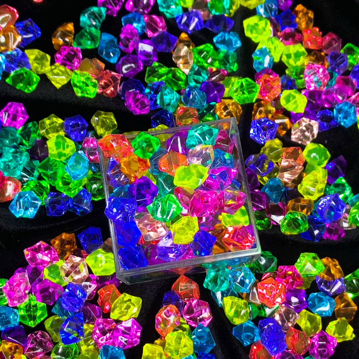 A colorful assortment of crystal ice cube acrylic stones in various shades of green, purple, blue, and pink scattered on a bl
