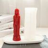 A red silicone mold shaped like a realistic human figure stands next to a white pillar candle.