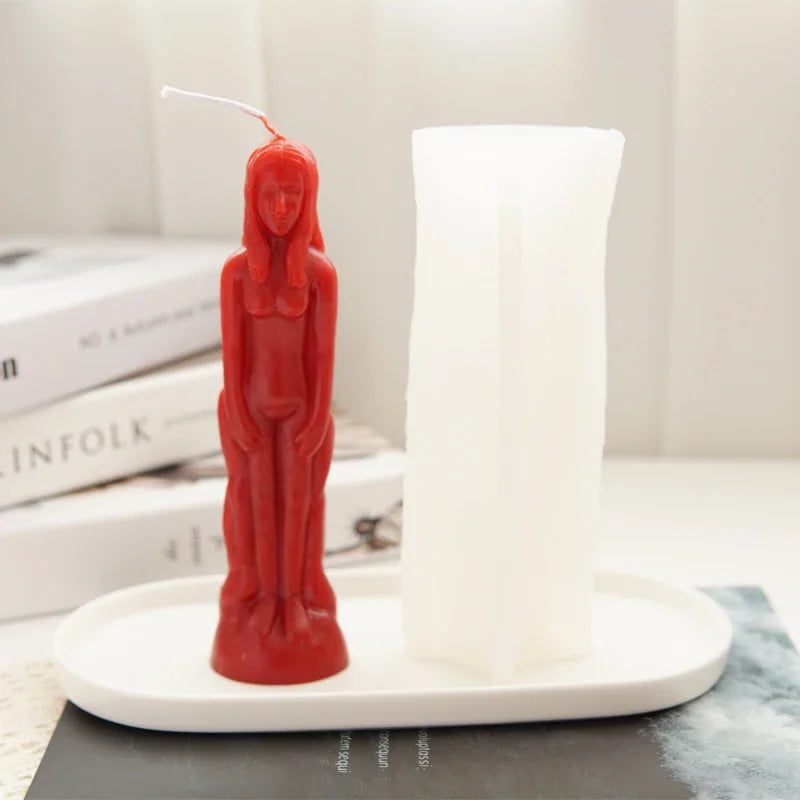 A red silicone mold shaped like a realistic human figure stands next to a white pillar candle.