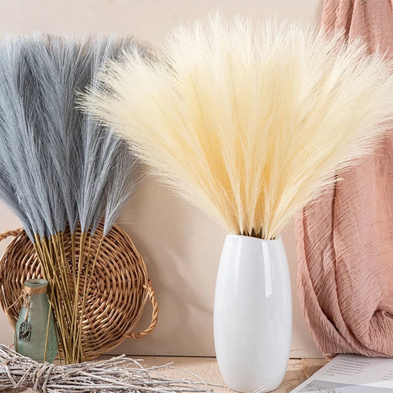 A bundle of fluffy, light yellow artificial pampas grass stems in a white vase against a neutral background.