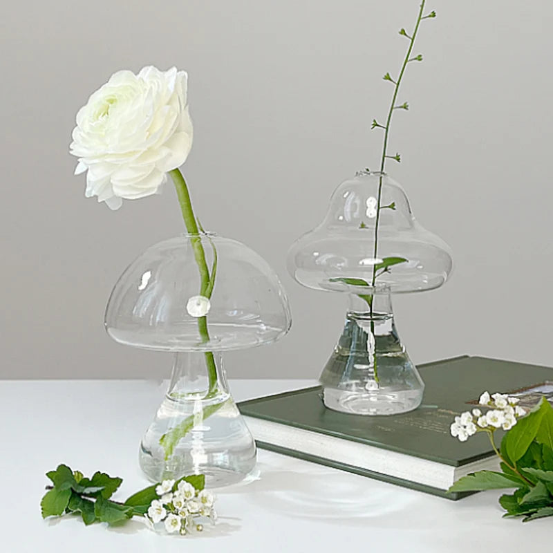 Vase décoratif en verre clair avec une rose blanche et une tige verte sur une surface blanche.