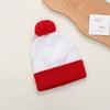 A festive knitted beanie with a red pom-pom and a matching red cuff is shown next to a wooden paddle.