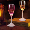 Un verre haut à pied rempli d'un liquide rose et or pétillant, posé sur une surface en bois à côté d'un livre.