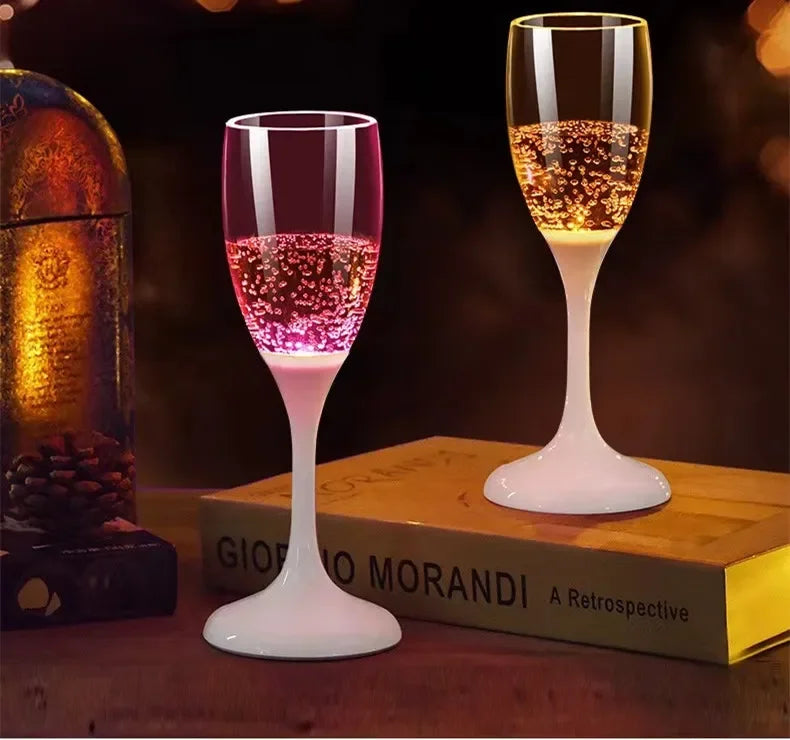 Un verre haut à pied rempli d'un liquide rose et or pétillant, posé sur une surface en bois à côté d'un livre.
