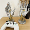 A silver and gold hand sculpture is displayed next to a white game controller on a wooden surface.