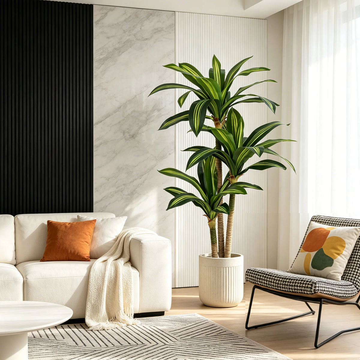 A tall artificial Dracaena tree in a white pot stands next to a modern sofa and a chair in a bright, minimalist living room.