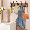 A wooden wall-mounted coat rack with five triple hooks displaying a pair of jeans and a straw hat.