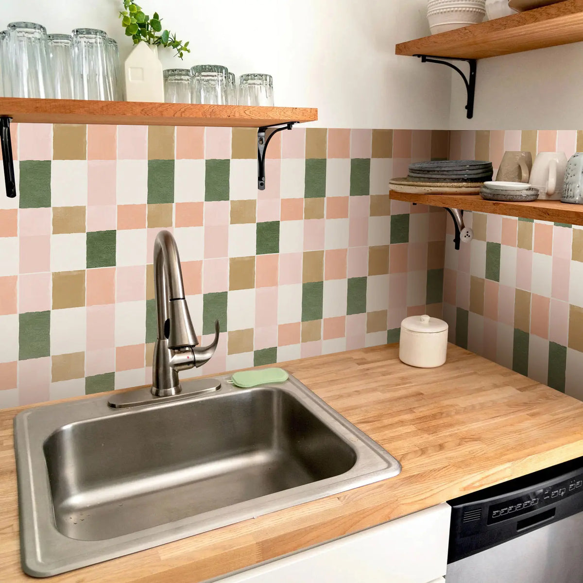 A kitchen sink and countertop with a pink and green tile backsplash and wooden shelves.