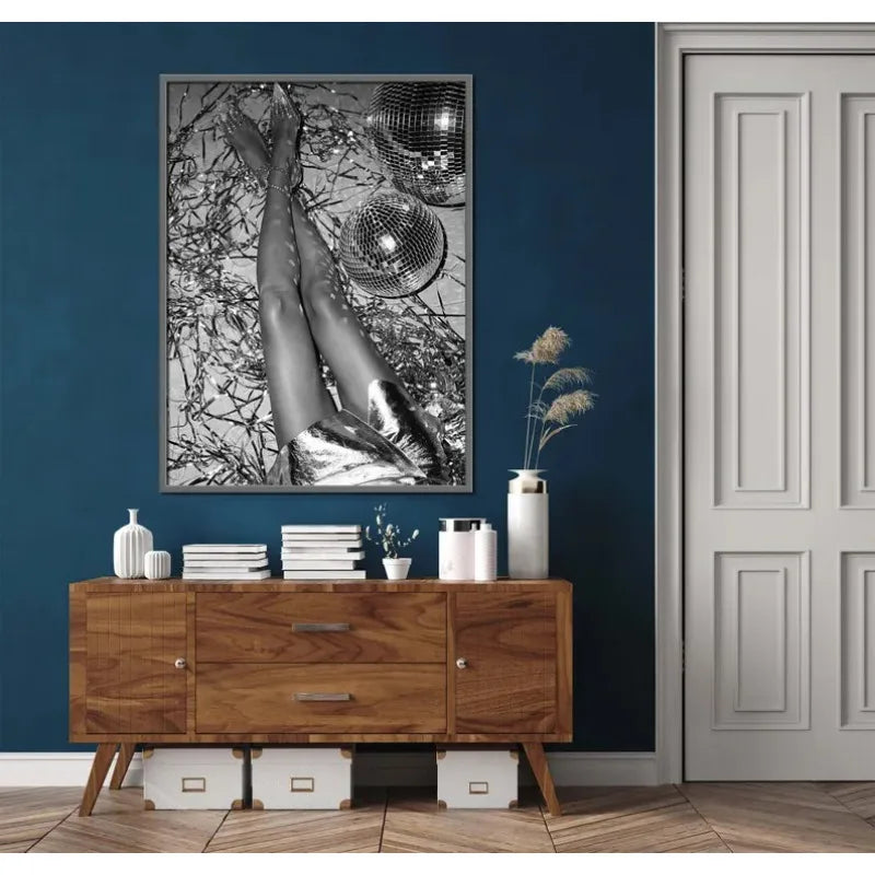 A framed canvas art piece featuring a black and white image of legs with leopard print texture hanging on a dark blue wall.