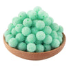 A pile of light green textured resin beads for jewelry making in a wooden bowl.