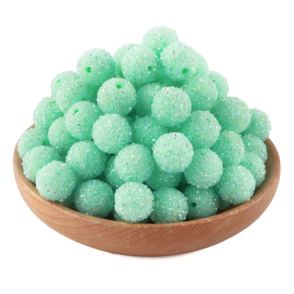 A pile of light green textured resin beads for jewelry making in a wooden bowl.