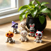 A set of Halloween resin figurines depicting a mummy, a skeleton, and a rabbit on a wooden surface next to a potted green pla