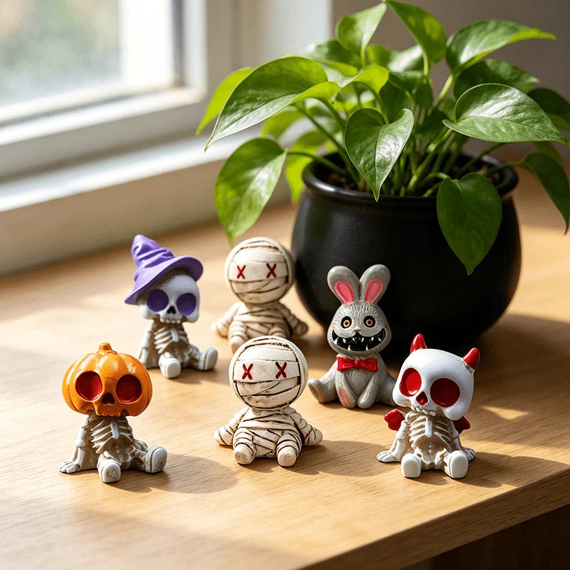 A set of Halloween resin figurines depicting a mummy, a skeleton, and a rabbit on a wooden surface next to a potted green pla