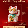 A white ceramic lucky cat ornament with gold-rimmed glasses sitting on a red base.