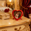 A red heart-shaped photo frame ornament displayed on a gilded dresser next to a pearl box.