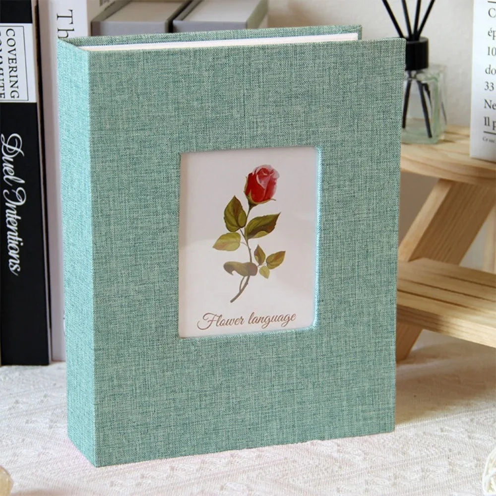 A square linen cover photo album in sage green with a floral design, displayed on a wooden surface.