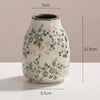 A handmade ice crackle ceramic vase with a speckled white glaze and green floral pattern.