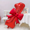 A large red foil balloon shaped like a heart with a matching bow, displayed on a white table.